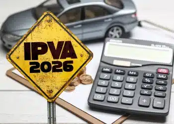 Placa amarela com a inscrição “IPVA 2026”, ao lado de uma calculadora, moedas e um carro em miniatura sobre uma mesa.