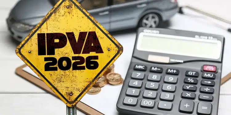 Placa amarela com a inscrição “IPVA 2026”, ao lado de uma calculadora, moedas e um carro em miniatura sobre uma mesa.