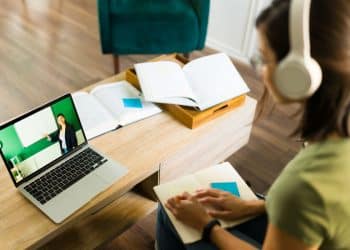Estudante assistindo aula online em uma faculdade EaD, com laptop e fones de ouvido, representando a flexibilidade do ensino a distância no Brasil.
