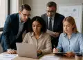 Equipe de quatro pessoas em reunião de trabalho analisando informações em um laptop.