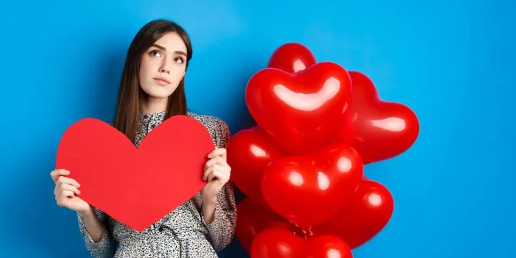 Mulher segurando coração de papel vermelho, ao lado de balões vermelhos em forma de coração, simbolizando o amor como chave para a felicidade.
