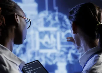 Duas pessoas analisando projeção de dados digitais em tela azul com tablet em mãos