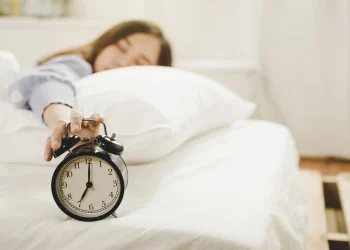 Pessoa deitada na cama apertando o despertador para adiar o alarme pela manhã.