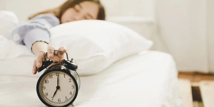 Pessoa deitada na cama apertando o despertador para adiar o alarme pela manhã.