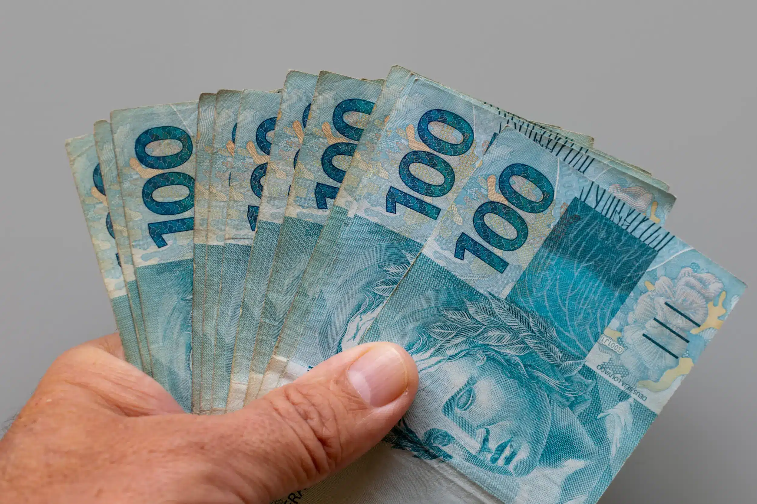 Notas de 100 reais em mãos, simbolizando os pagamentos do INSS com destaque para a segunda-feira, 02 de março.