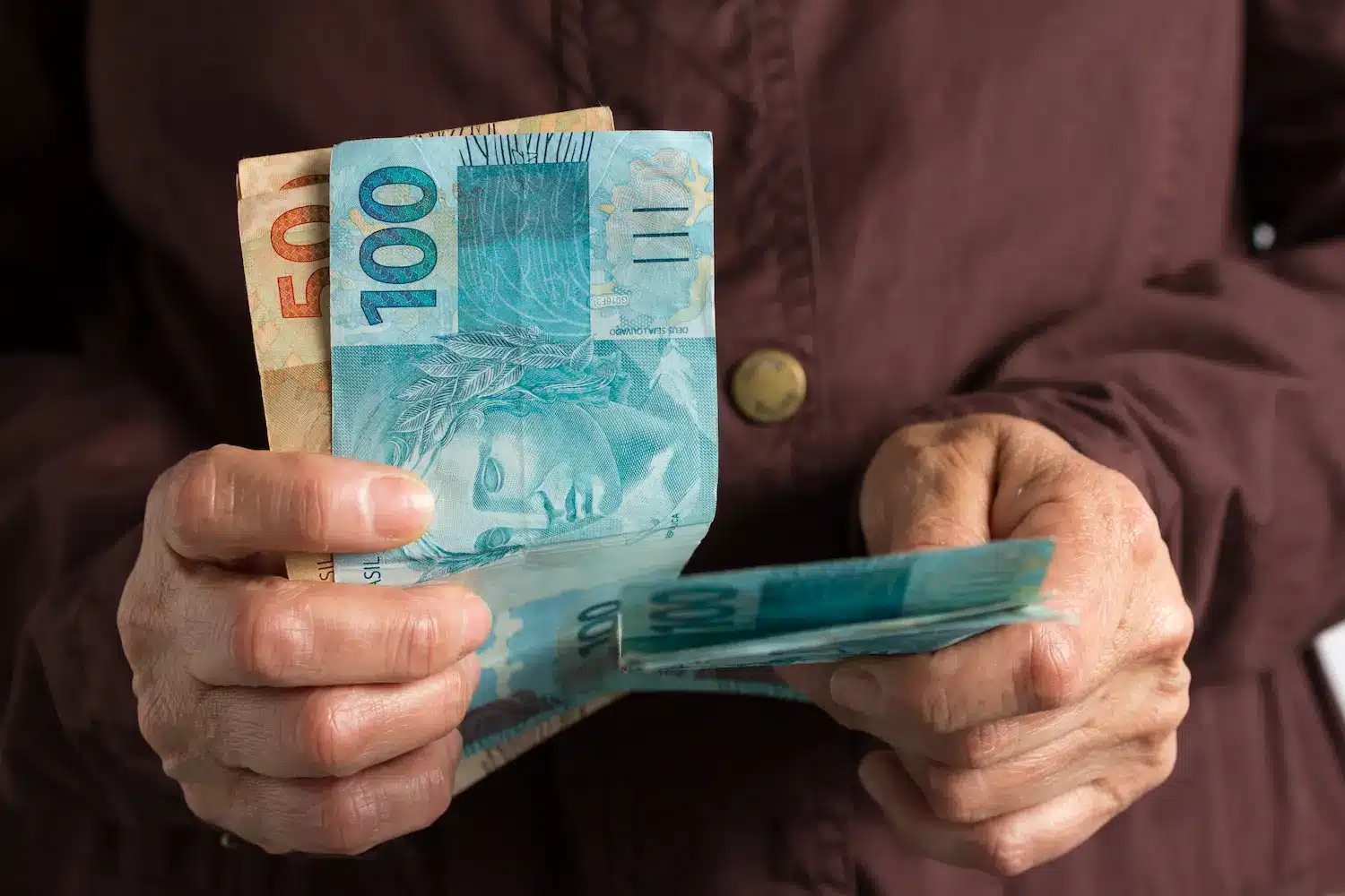 Pessoa segurando e contando notas de real, representando o recebimento de benefício previdenciário do INSS.