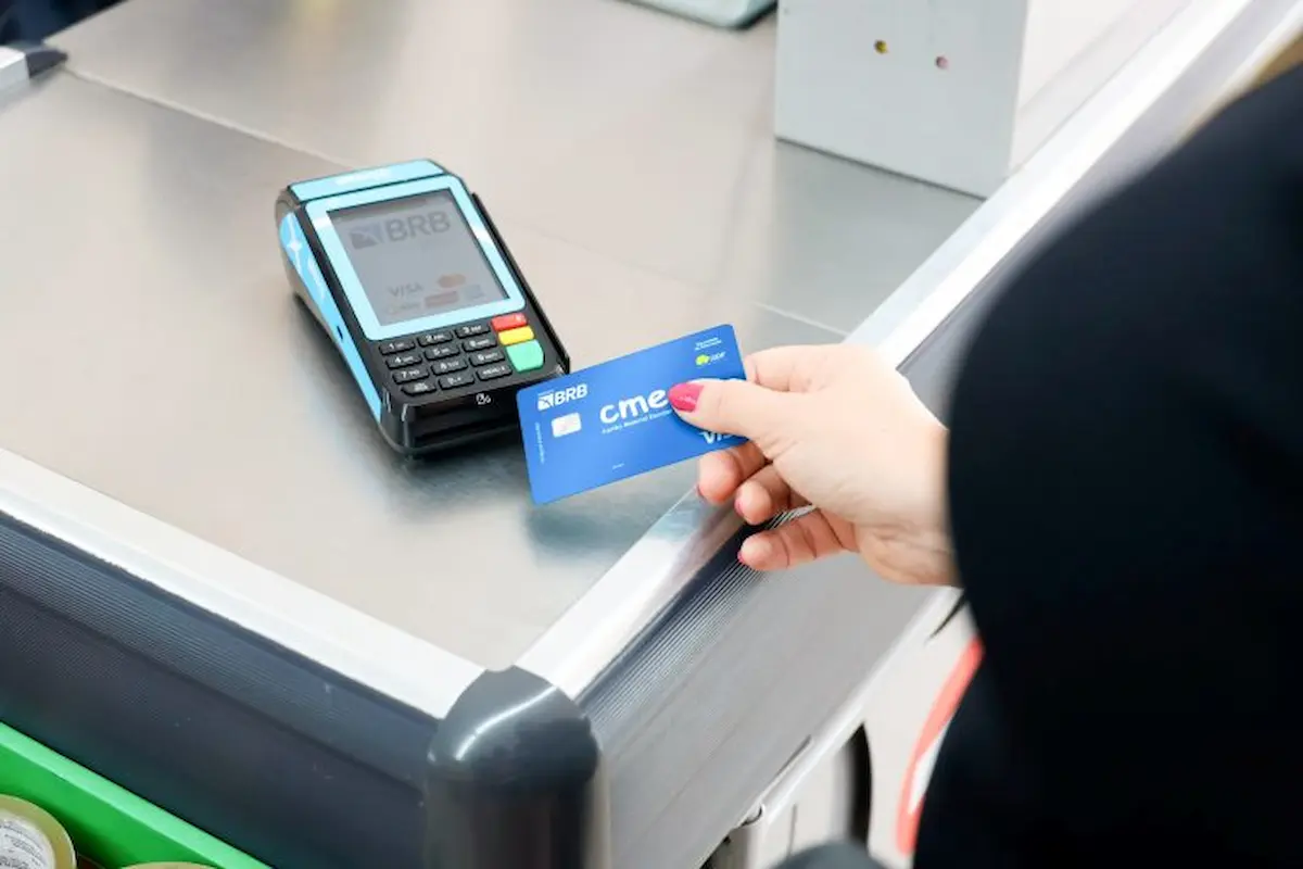 Pessoa realizando pagamento com cartão do programa de material escolar em terminal eletrônico no caixa de loja.
