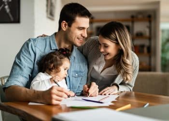 Família feliz planejando finanças juntos em casa com criança desenhando na mesa