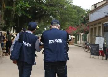 Dois recenseadores do IBGE caminham juntos em rua de vila para coleta de informações