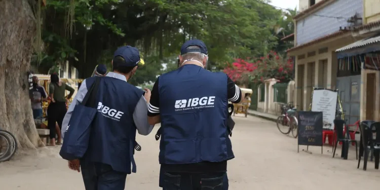 Dois recenseadores do IBGE caminham juntos em rua de vila para coleta de informações