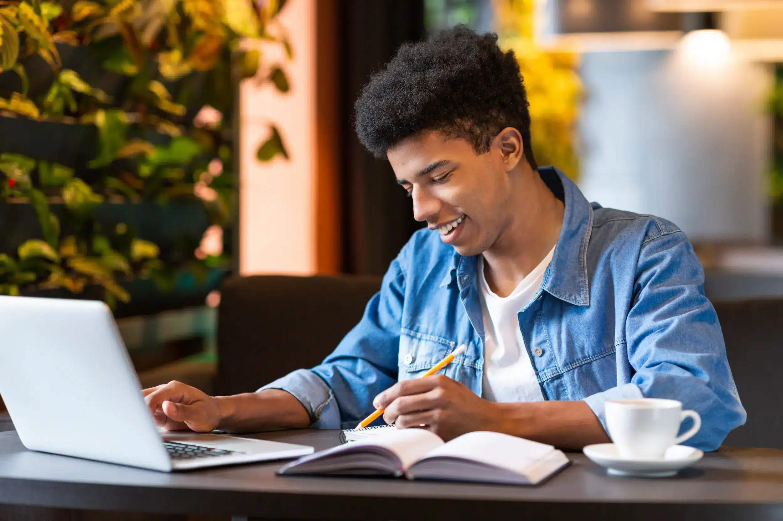 Jovem estudando com laptop e caderno, demonstrando foco e dedicação para aprovação em concursos.