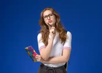 Jovem mulher pensando enquanto segura um caderno, refletindo sobre a escolha de um curso universitário entre bacharelado, licenciatura e tecnológico.