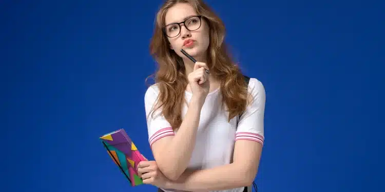 Jovem mulher pensando enquanto segura um caderno, refletindo sobre a escolha de um curso universitário entre bacharelado, licenciatura e tecnológico.