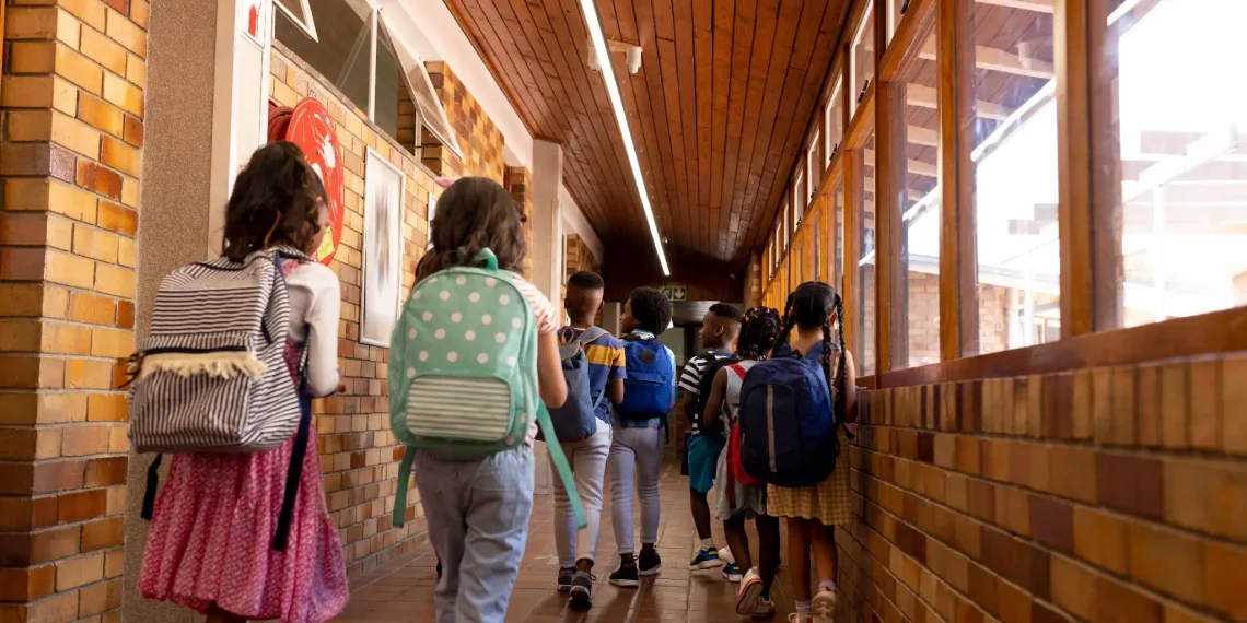 Crianças caminhando pelo corredor da escola com mochilas, simbolizando o retorno às aulas em 2026.