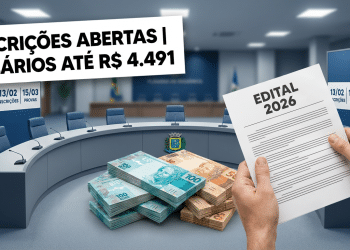 Duas mãos seguram edital 2026 diante de mesa redonda da câmara com pilhas de dinheiro