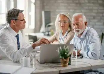 Homem de terno mostra informações no notebook para casal de idosos atentos em reunião