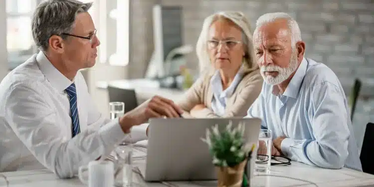 Homem de terno mostra informações no notebook para casal de idosos atentos em reunião