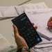 Mão segura celular com calculadora e outra faz anotações entre boletos