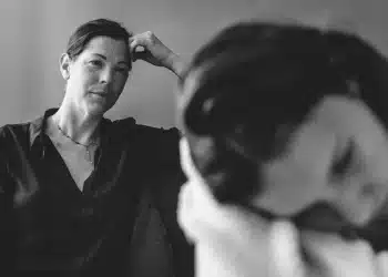 Mãe observa filha adolescente cabisbaixa durante conversa tensa em ambiente doméstico.