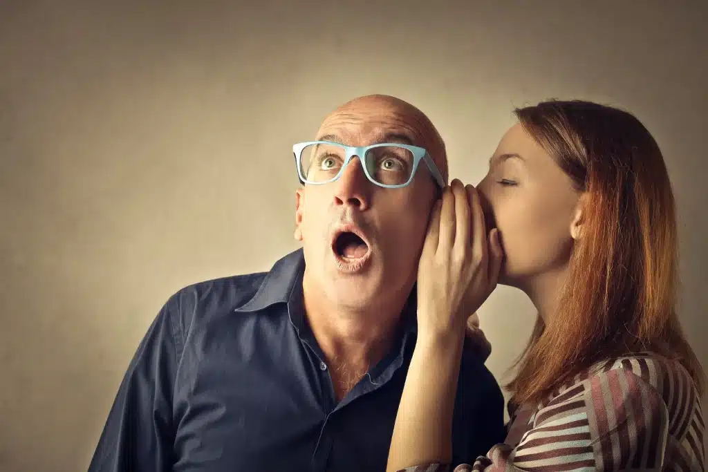 Pessoa sussurrando um segredo no ouvido de um homem surpreso, ilustrando o compartilhamento de informações pessoais em conversas privadas.