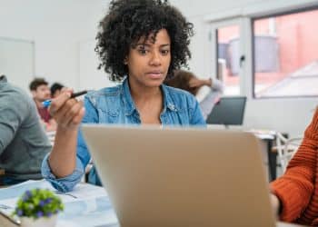 Estudante usando notebook em sala de aula para realizar inscrição em cursos gratuitos de qualificação profissional.