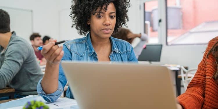 Estudante usando notebook em sala de aula para realizar inscrição em cursos gratuitos de qualificação profissional.