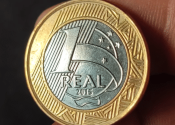 Foto em close do reverso de uma moeda de 1 real comemorativa das Olimpíadas Rio 2016, exibindo o valor "1 REAL" e o ano de cunhagem "2015" no centro do núcleo prateado.