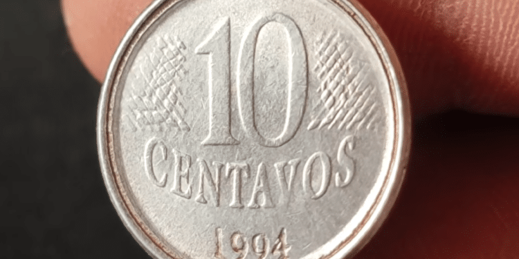 Close-up de uma moeda de 10 centavos de real do ano de 1994, feita de aço inox, sendo segurada pelos dedos de uma pessoa. A imagem foca no reverso, onde o número "10" e a palavra "CENTAVOS" estão centralizados, com a data "1994" logo abaixo. É possível notar detalhes da cunhagem e pequenos sinais de circulação.
