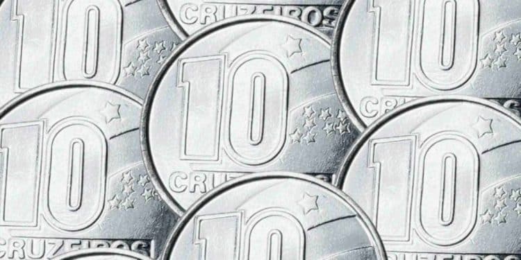 Close de várias moedas prateadas de 10 Cruzeiros sobrepostas em um plano detalhado. É possível ver claramente o número 10 e a palavra "CRUZEIROS" gravados em metal brilhante com estrelas ao fundo.