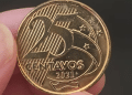 Close-up de uma moeda brasileira de 25 centavos do ano de 2021 sendo segurada, mostrando o valor e o ano em alto relevo, ideal para identificação de erros.