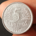 Close frontal de uma moeda prateada de 5 centavos do ano 1997, mostrando o algarismo central e a textura de linhas inclinadas ao fundo.