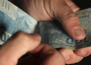 Beneficiário contando cédulas de R$ 100 representando antecipação do 13º salário do INSS que injeta R$ 78 bilhões na economia