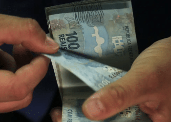 Mãos contando cédulas de cem reais representando os pagamentos de fevereiro do PIS Pasep e Pé-de-Meia