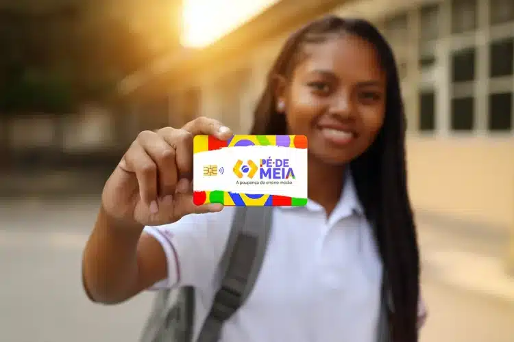 Estudante sorridente segura cartão colorido do Pé-de-Meia próximo à câmera