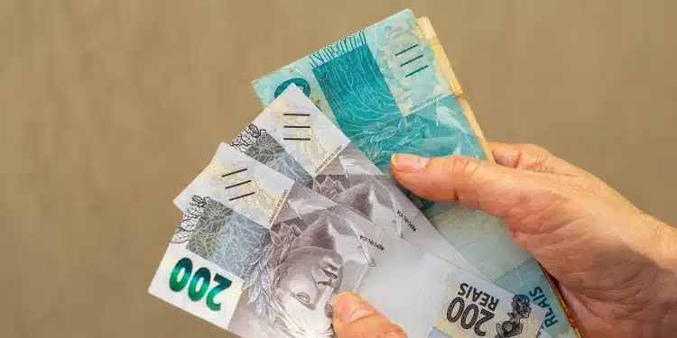Notas de 200 reais em mãos, representando a nova rodada de pagamentos do INSS, com foco no valor e a distribuição dos benefícios.