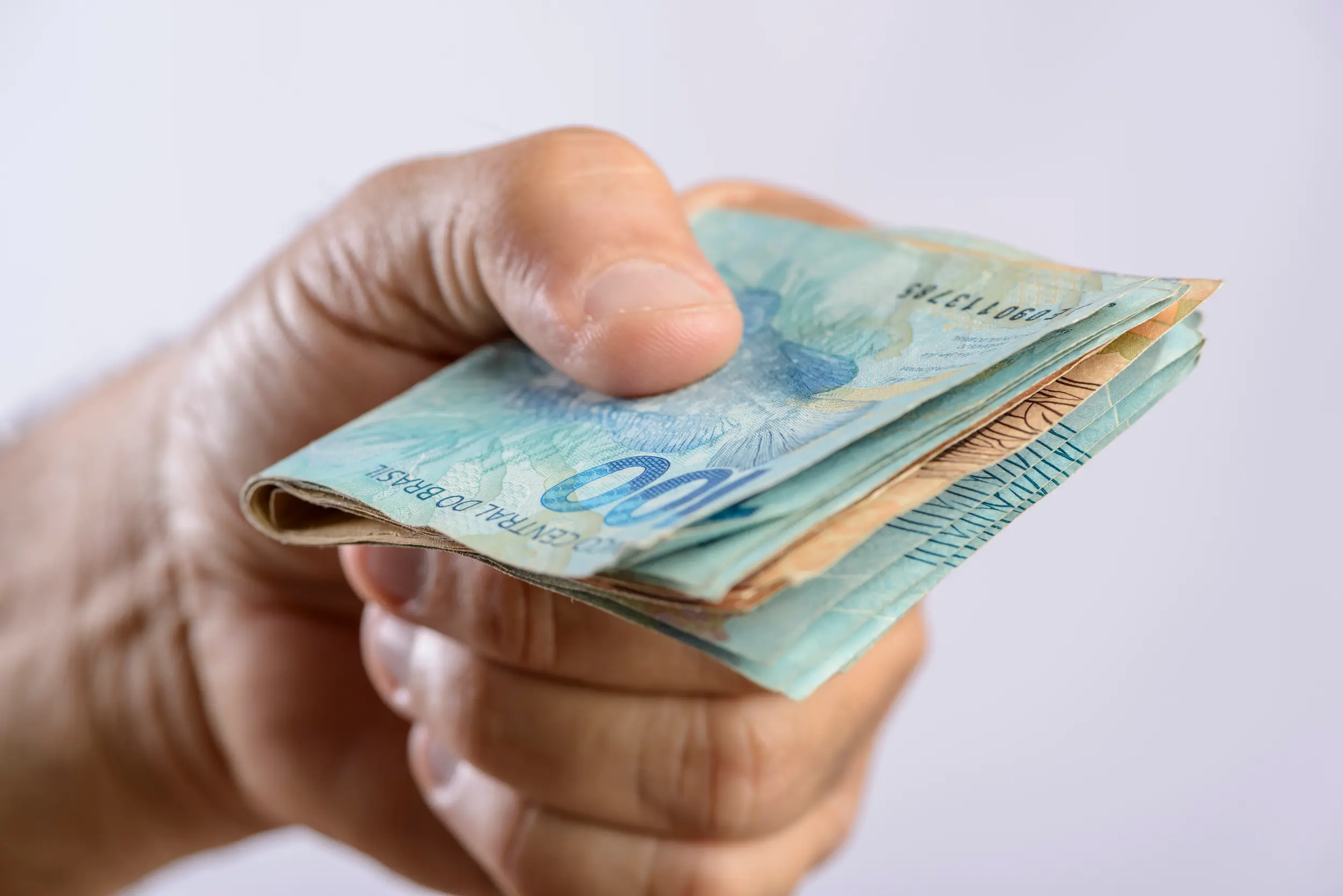 Pessoa segurando cédulas de R$ 100, representando valores do Pé-de-Meia que podem ser retirados ou retidos.