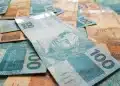 Notas de dinheiro brasileira, com destaque para a cédula de R$ 100 e R$ 50, representando valores de auxílio financeiro para o programa Pé-de-Meia 2026.