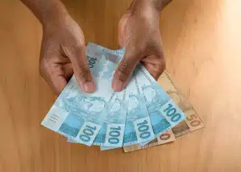 Notas de cem e cinquenta reais sendo seguradas com as mãos, representando o pagamento do INSS disponível em fevereiro de 2026.