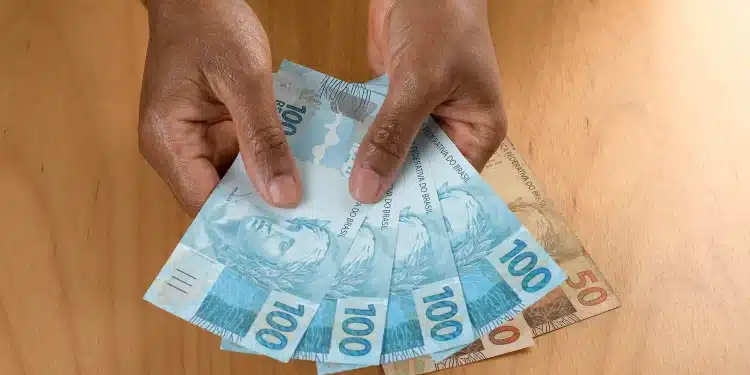 Notas de cem e cinquenta reais sendo seguradas com as mãos, representando o pagamento do INSS disponível em fevereiro de 2026.