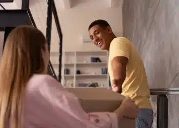 Pessoa sorrindo e ajudando outra a carregar uma caixa, representando gentileza e felicidade.