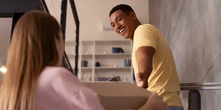 Pessoa sorrindo e ajudando outra a carregar uma caixa, representando gentileza e felicidade.