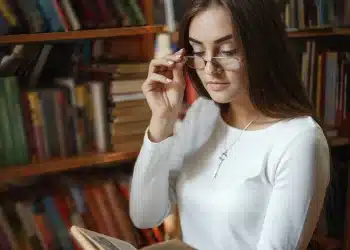 Mulher lendo livro em biblioteca, refletindo sobre frases de inteligência.