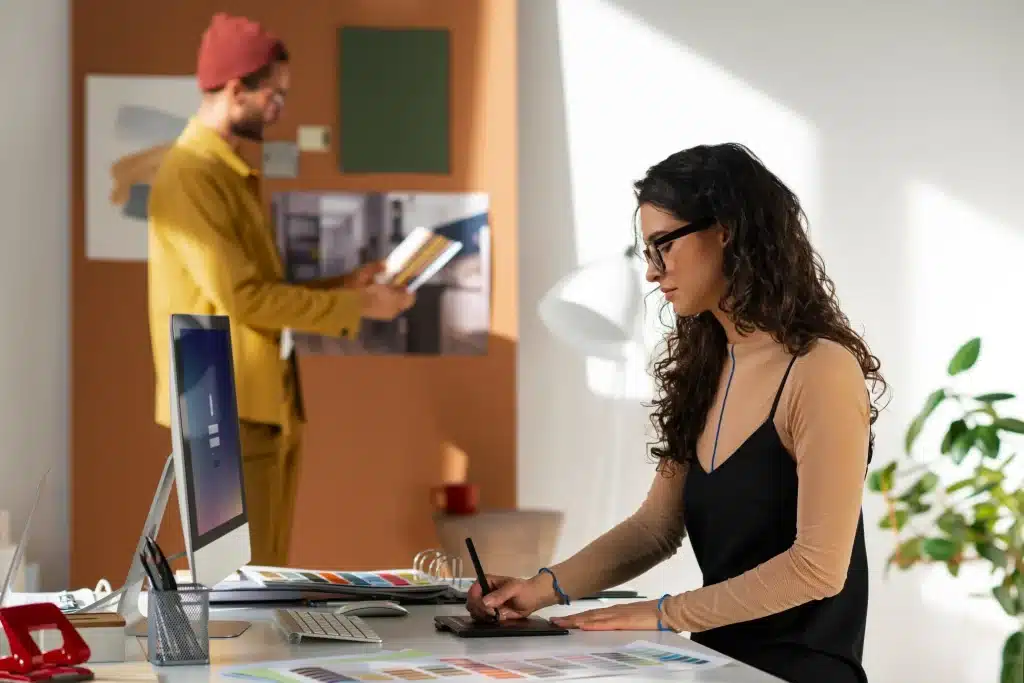 Designer gráfico criando identidade visual em mesa digitalizadora com referências de cores no escritório.