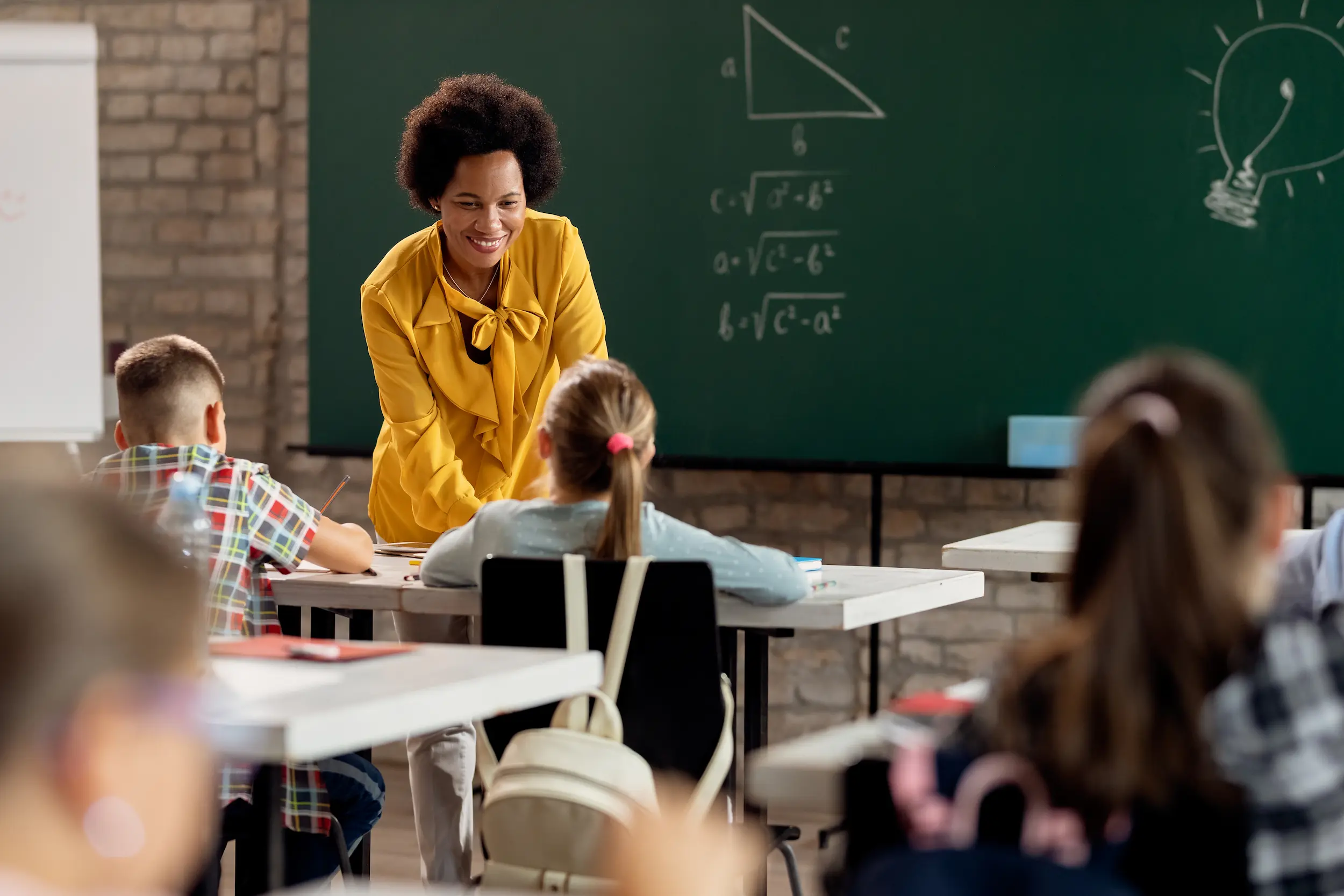 Professora sorridente interagindo com seus alunos em uma sala de aula, abordando conteúdos de aprendizagem.