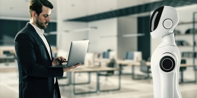 Profissional utilizando notebook diante de robô humanoide em escritório moderno, representando a colaboração entre inteligência artificial e habilidades humanas no mercado de trabalho.