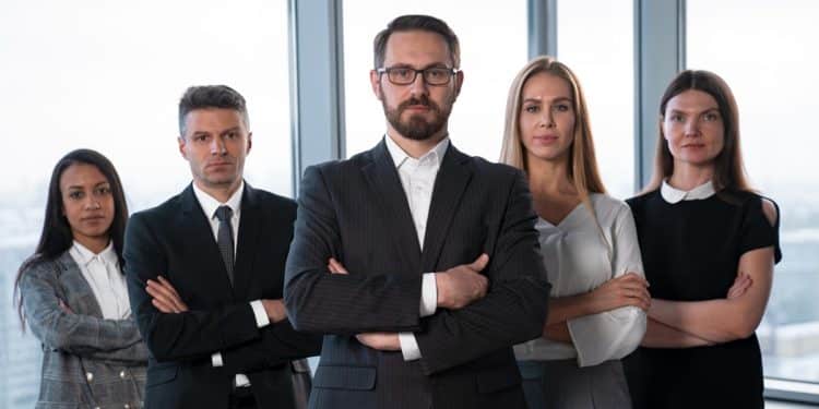 Grupo de cinco executivos de braços cruzados em escritório representando profissões CLT bem remuneradas no Brasil.