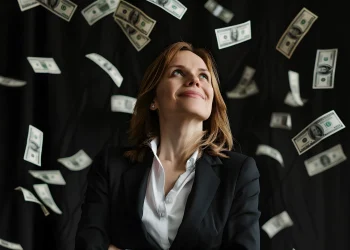 Mulher executiva sorrindo enquanto notas de dólar caem ao redor, simbolizando carreiras de alta remuneração.