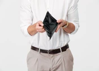 Homem vestindo camisa branca segurando uma carteira preta aberta e vazia, simbolizando a crise financeira e baixos salários.