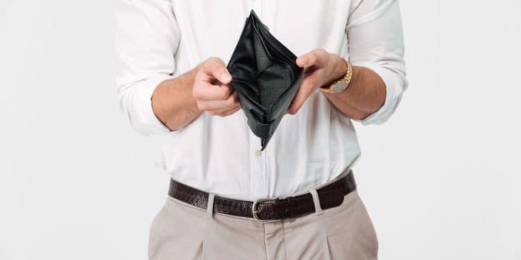 Homem vestindo camisa branca segurando uma carteira preta aberta e vazia, simbolizando a crise financeira e baixos salários.
