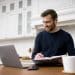Homem sorrindo trabalhando em home office com laptop fone de ouvido e caderno representando profissões remotas bem remuneradas